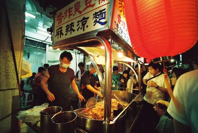 身穿黑色围裙和面具的男子在街上食物区烹调食物